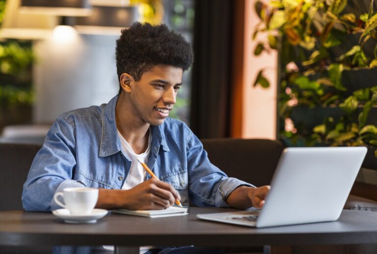 conseguir clientes como freela - a imagem mostra um homem jovem trabalhando em frente a um computador, em um ambiente descontraído. Ele é negro, usa uma camisa azul sorri,